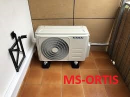 Biała jednostka zewnętrzna klimatyzatora marki Kaisai, ustawiona na czarnych podkładkach antywibracyjnych na brązowej, wykafelkowanej podłodze balkonu, z widocznym uchwytem montażowym na ścianie.