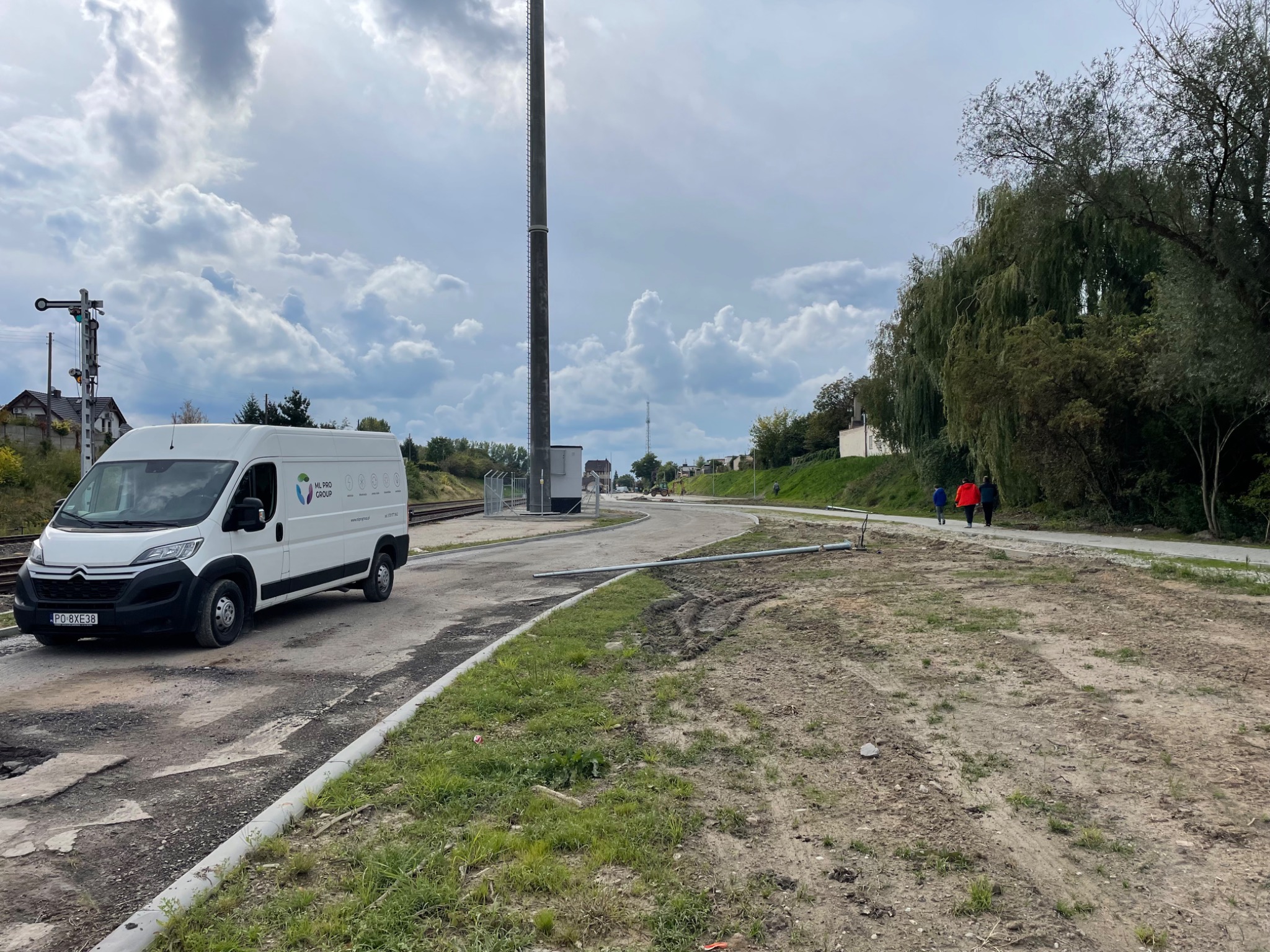 Przygotowanie terenu pod utwardzenie drogi w Kostrzynie: biały samochód dostawczy na placu budowy, widoczna droga w trakcie budowy, maszt telekomunikacyjny w tle.