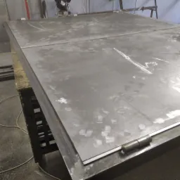 Surowe, metalowe płyty ułożone na stole roboczym, prawdopodobnie w trakcie przygotowania do dalszej obróbki lub spawania, z widocznymi śladami wcześniejszych prac.