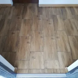 Ułożona podłoga z płytek imitujących drewno w przedpokoju, widok z góry, z widocznymi fugami i listwami przypodłogowymi.