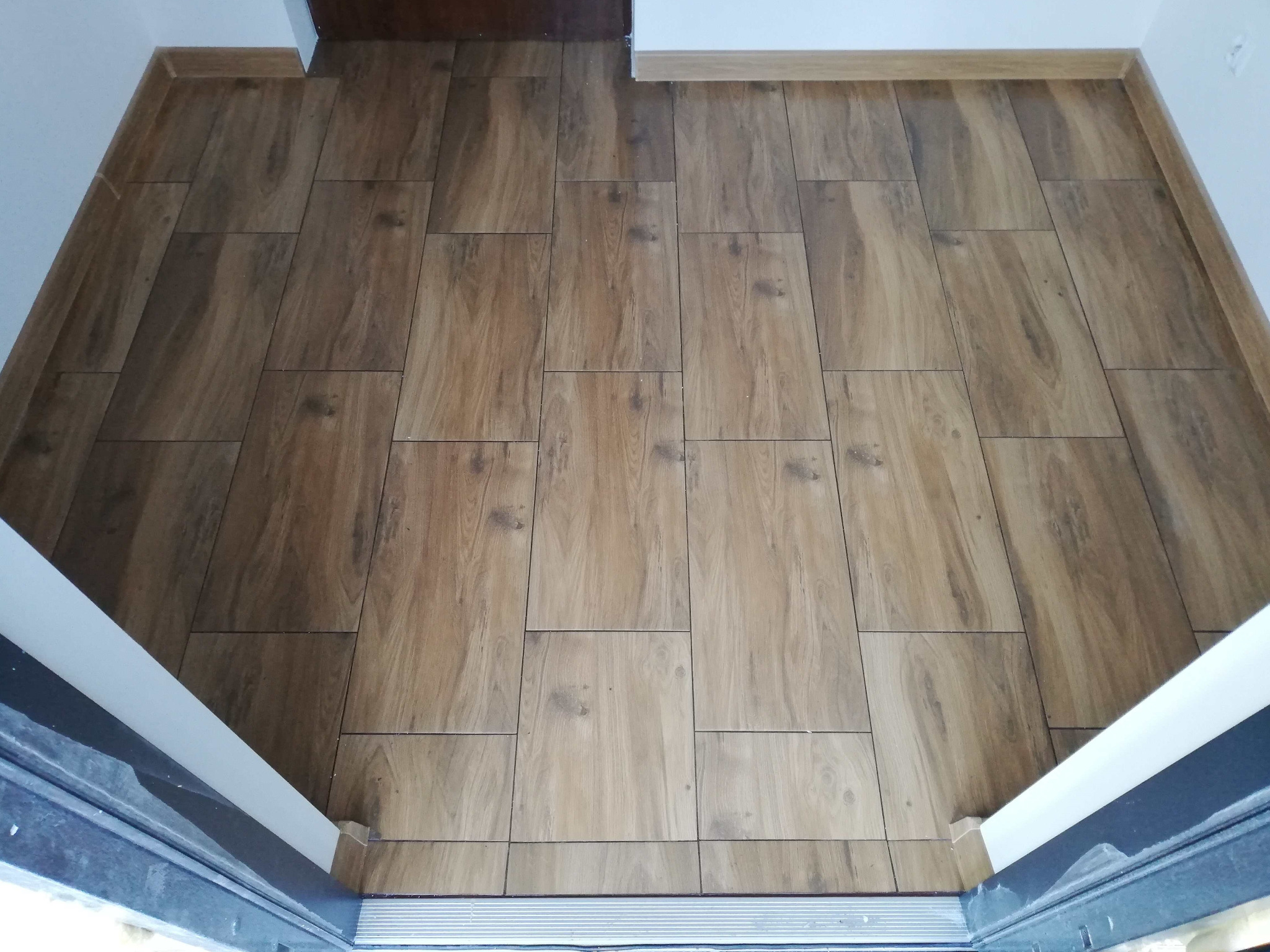 Ułożona podłoga z płytek imitujących drewno w przedpokoju, widok z góry, z widocznymi fugami i listwami przypodłogowymi.