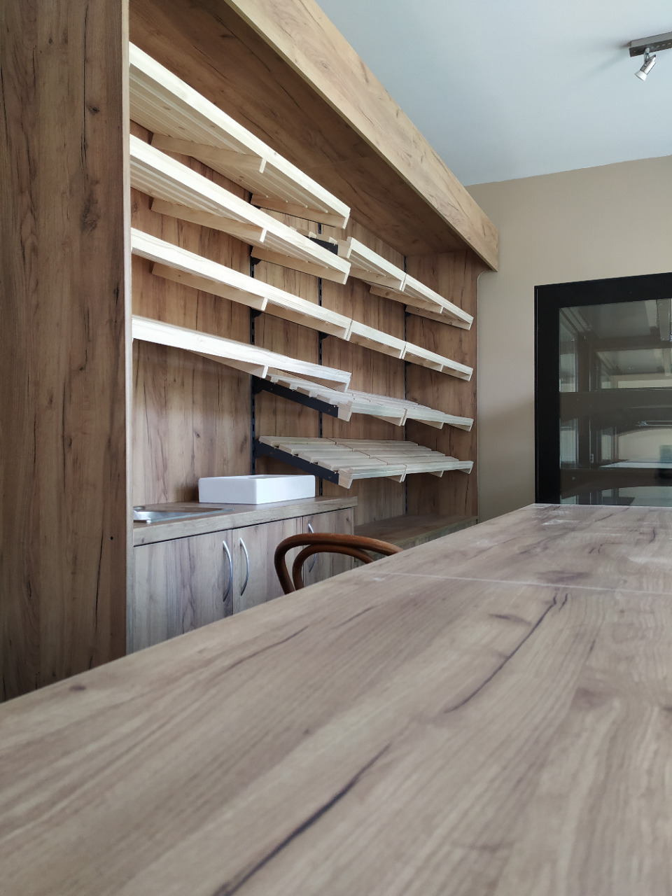 Kuchenne półki z surowego drewna, zamontowane na ścianie z drewnopodobną okleiną, widoczne z perspektywy blatu z podobnym wykończeniem, z umywalką w tle.