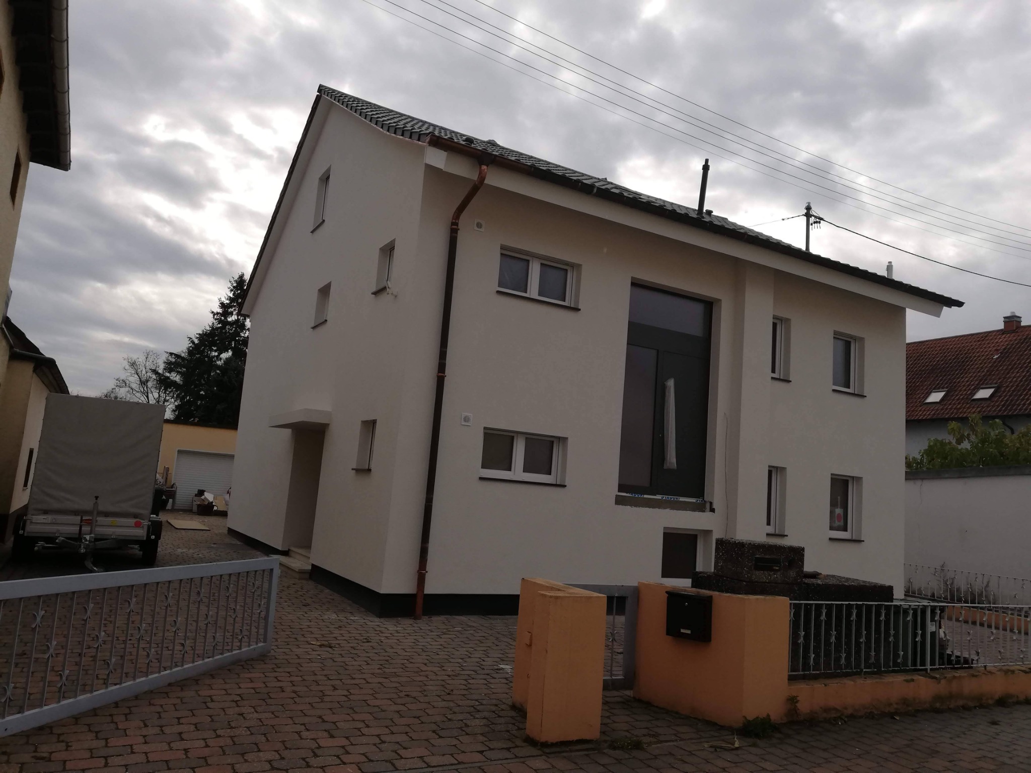 Dwupiętrowy dom jednorodzinny z ocieploną elewacją, widoczny z zewnątrz, z nowymi oknami i rynnami, na tle pochmurnego nieba.