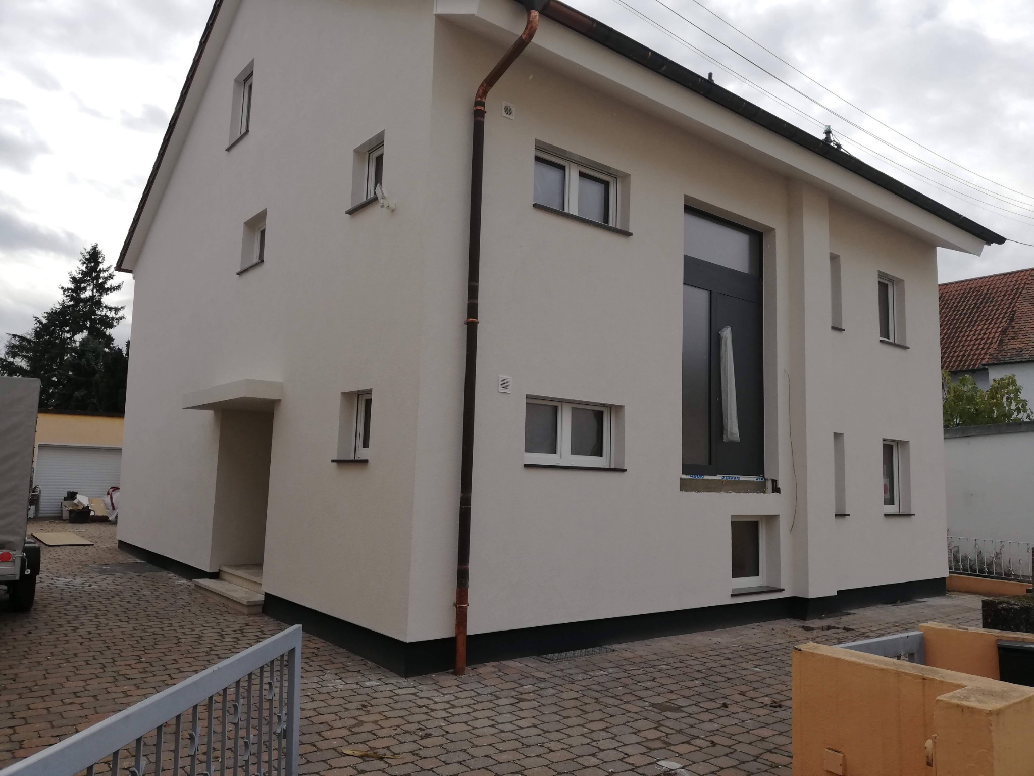 Dwukondygnacyjny dom jednorodzinny z jasną elewacją po ociepleniu, widoczny fragment rynny, okna z ciemnymi ramami, kostka brukowa na podwórku.