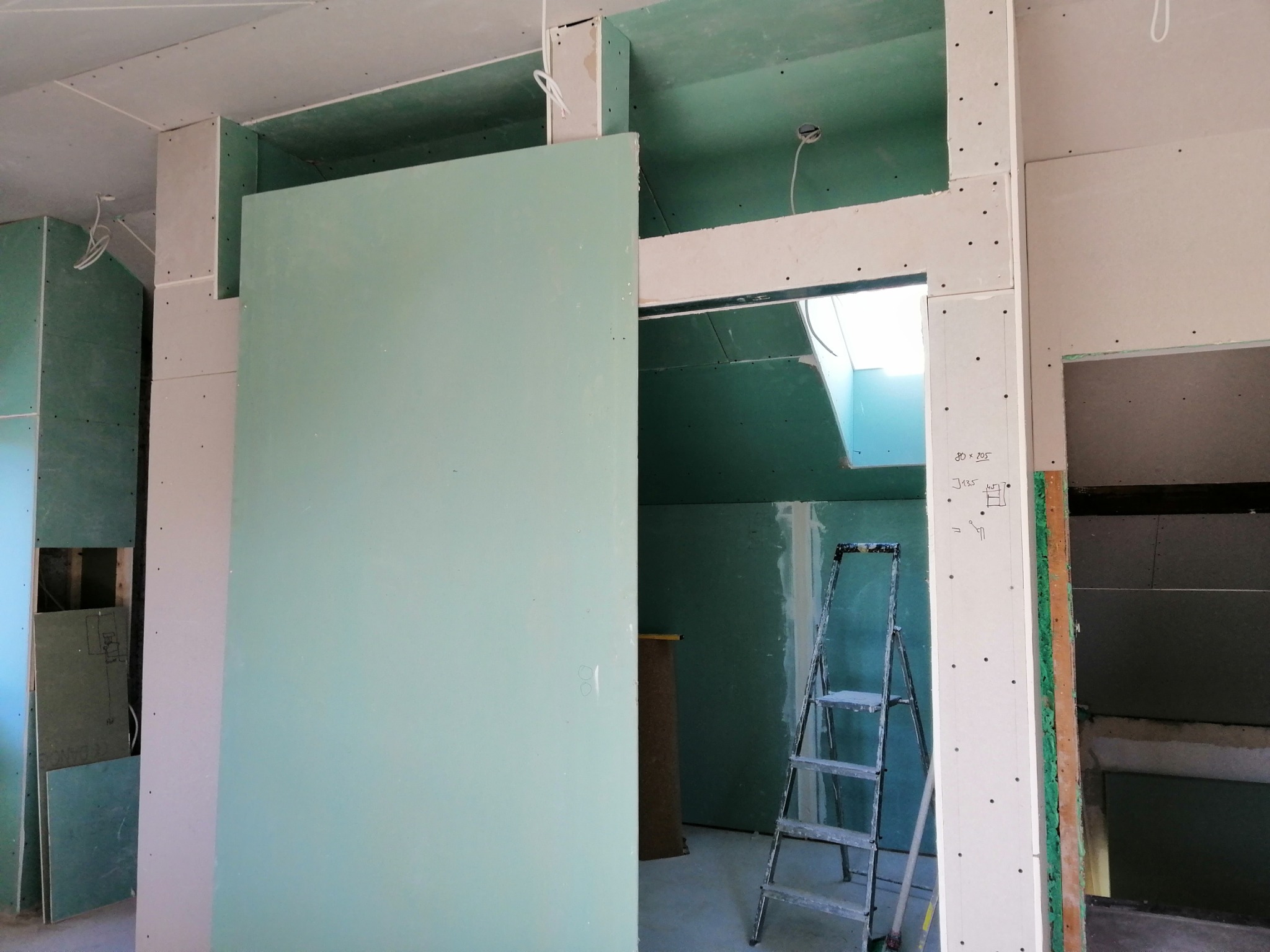 Wnętrze w trakcie prac wykończeniowych: ściany i sufit pokryte płytami gipsowo-kartonowymi, widoczne profile, drabina aluminiowa, instalacja elektryczna wyprowadzona ze ściany.