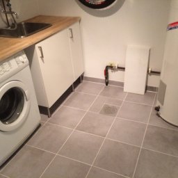 Konrad Stępień - Wykończona łazienka z szarymi płytkami podłogowymi, pralką AEG, szafką z drewnianym blatem i bojlerem elektrycznym