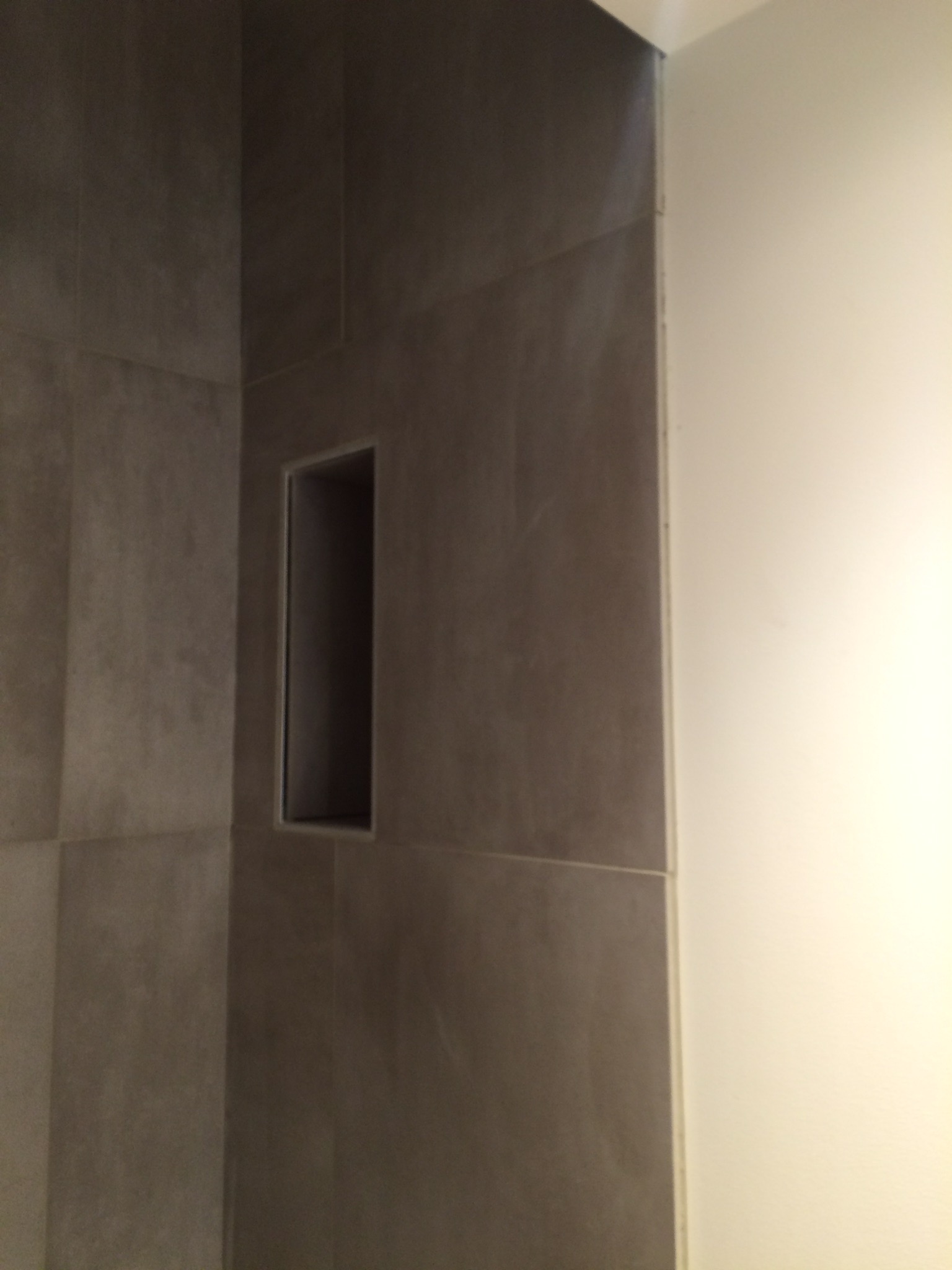 Fragment ściany łazienki wyłożonej szarymi płytkami z wnęką, widok z bliska na narożnik i styk z białą ścianą.