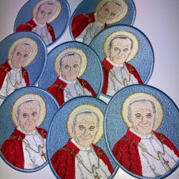 Studio RS Haft Komputerowy - Owalne naszywki z haftowanym portretem papieża Jana Pawła II w czerwonej szacie, otoczonego aureolą, na błękitnym tle. Widoczne detale haftu i złoty łańcuszek z krzyżem.