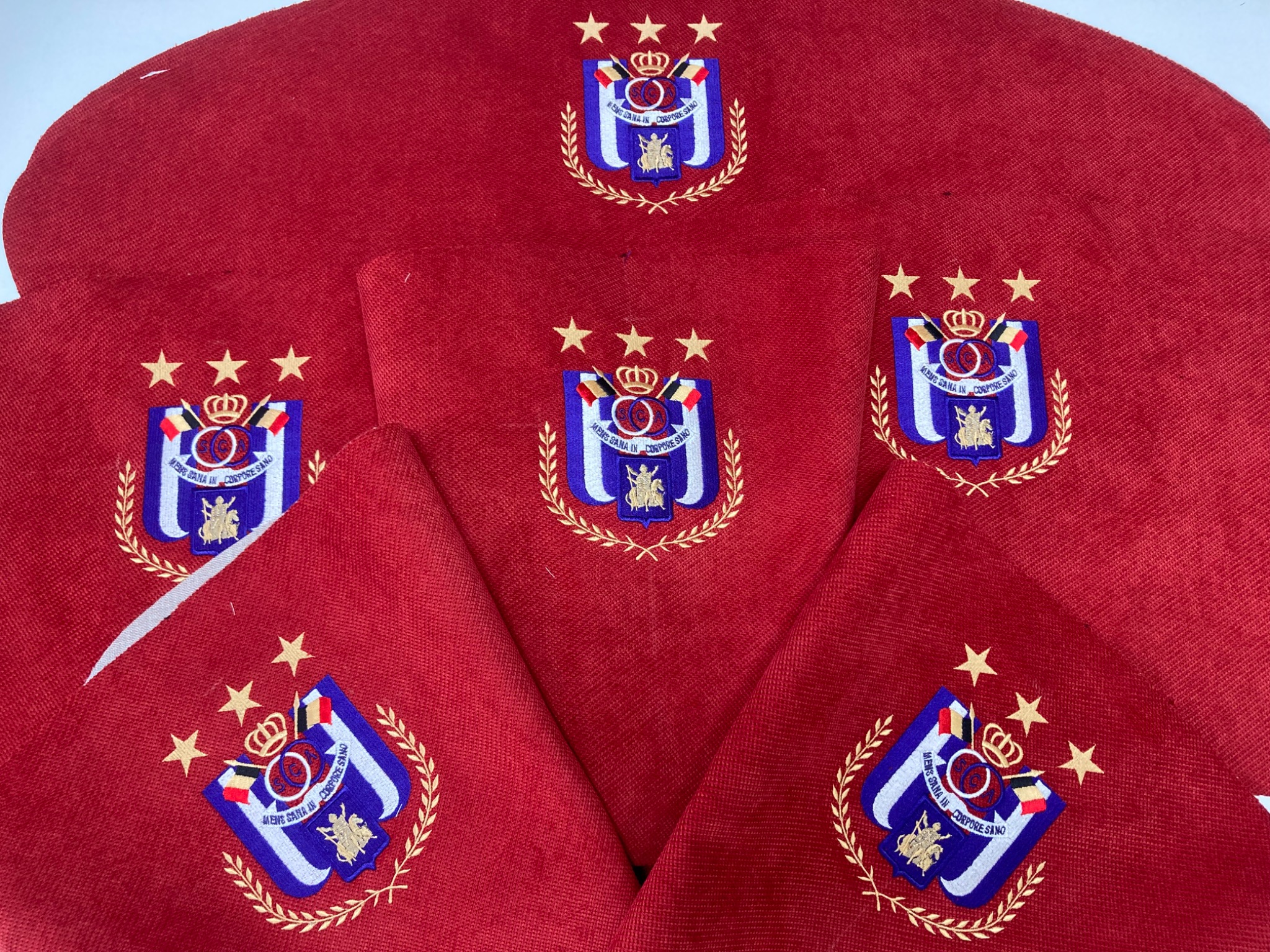 Czerwone berety z wyhaftowanym herbem z trzema gwiazdami ułożone warstwami.