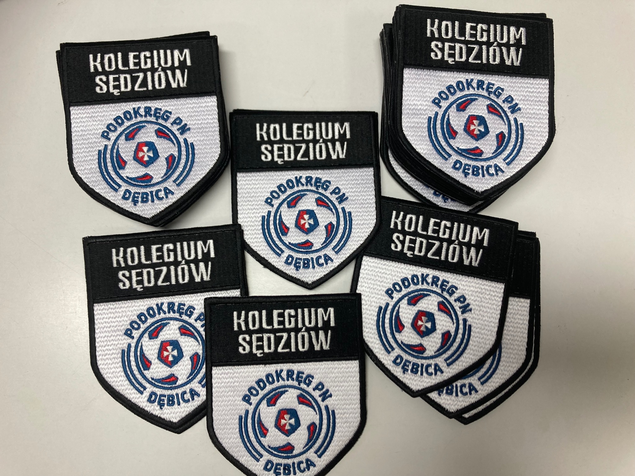 Naszywki z logo 'Kolegium Sędziów Podokręg PN Dębica' ułożone na białym tle. Detaliczne wykonanie, widoczna faktura materiału i precyzyjne szwy.