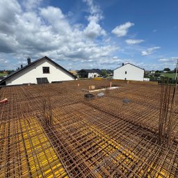 ARMBET Vasyl Bersan - Zbrojenie stropu na żółtym szalunku, widok z góry na konstrukcję z prętów stalowych, w tle budynki mieszkalne i błękitne niebo z chmurami.