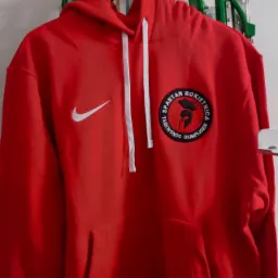 Czerwona bluza z kapturem, z białym logo Nike i naszywką 'Spartan Rokietnica Taekwondo Olimpijskie' z motywem hełmu spartańskiego.