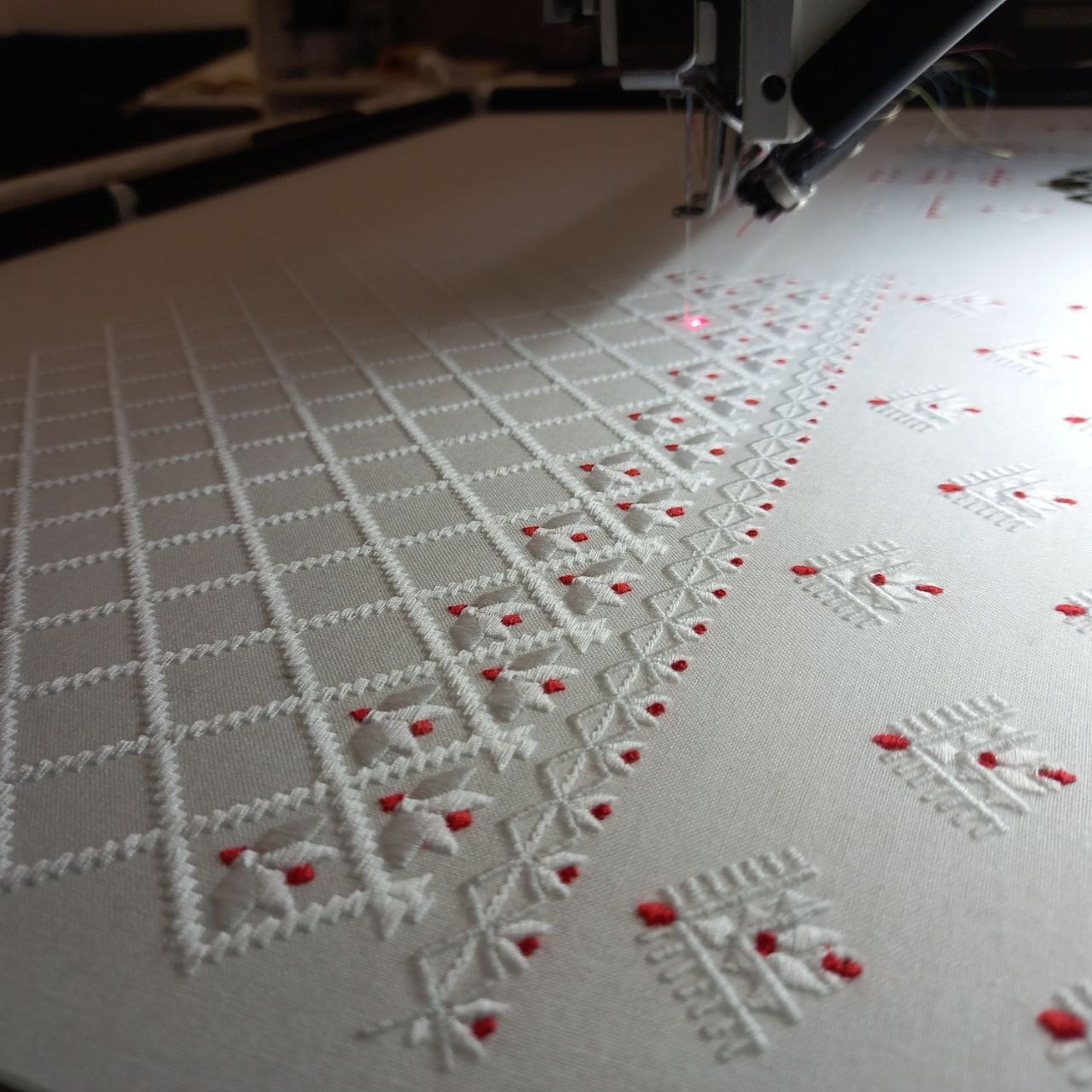 Automatyczna maszyna wykonuje biało-czerwony wzór na białym materiale, widoczna igła i laserowy wskaźnik