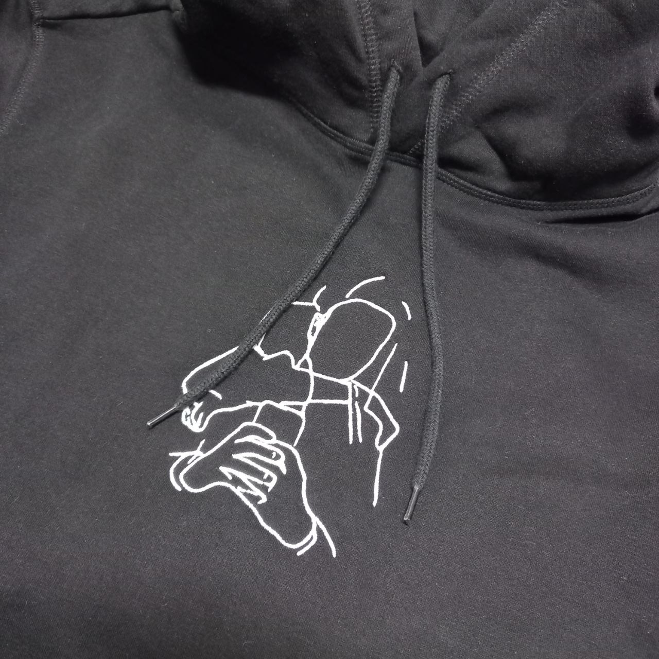 Czarna bluza z kapturem z białym, minimalistycznym haftem przedstawiającym osobę trzymającą telefon.