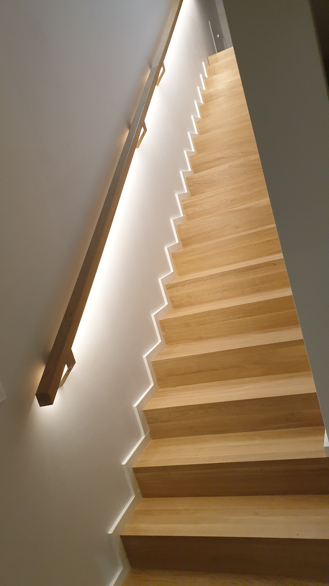Nowoczesne schody z jasnego drewna z podświetleniem LED wzdłuż stopni i drewnianą poręczą.