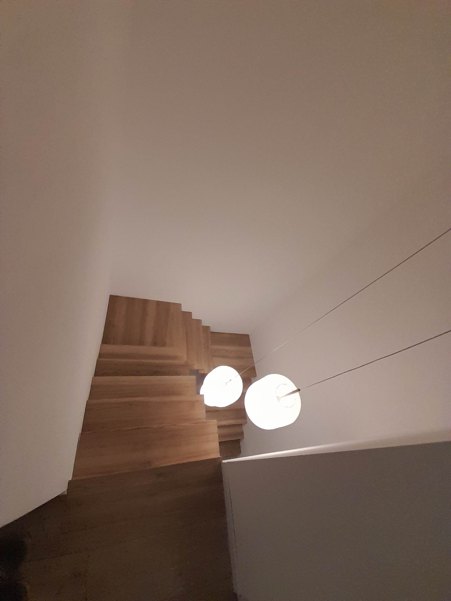 Widok z góry na drewniane schody z oświetleniem wiszącym, minimalistyczny design, jasne drewno i białe ściany.