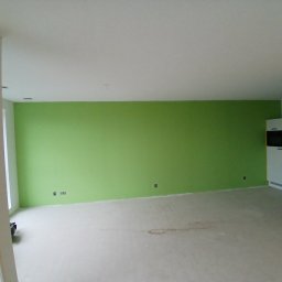 Fende Schilderwerken - Wnętrze po remoncie: ściana pomalowana na zielono, jasna podłoga, widoczne gniazdka elektryczne, fragment zabudowy kuchennej z krzesłem barowym.