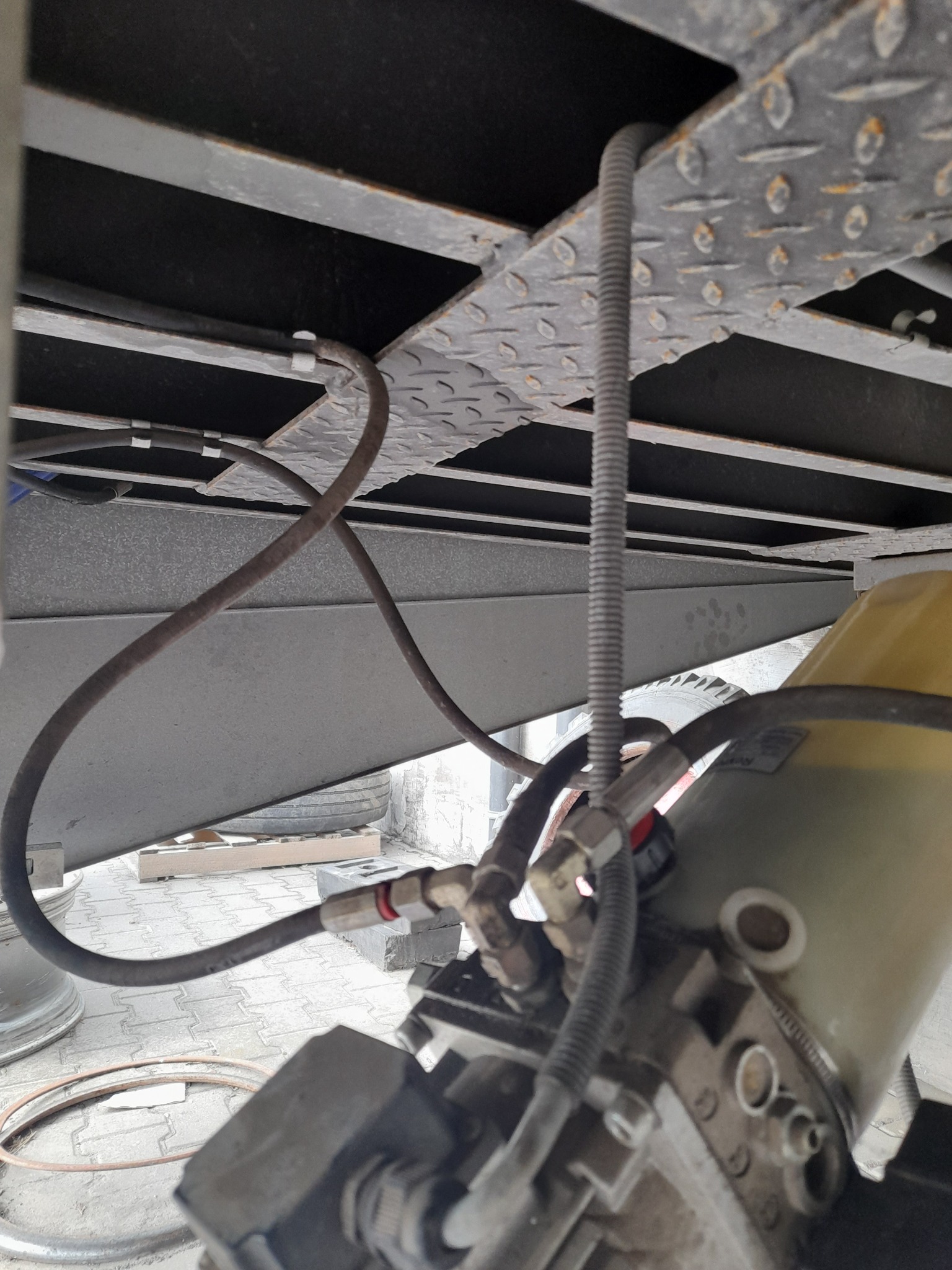 Szczegółowe ujęcie hydraulicznego siłownika bramy przemysłowej z widocznymi przewodami i elementami montażowymi, zamocowanego pod konstrukcją bramy.