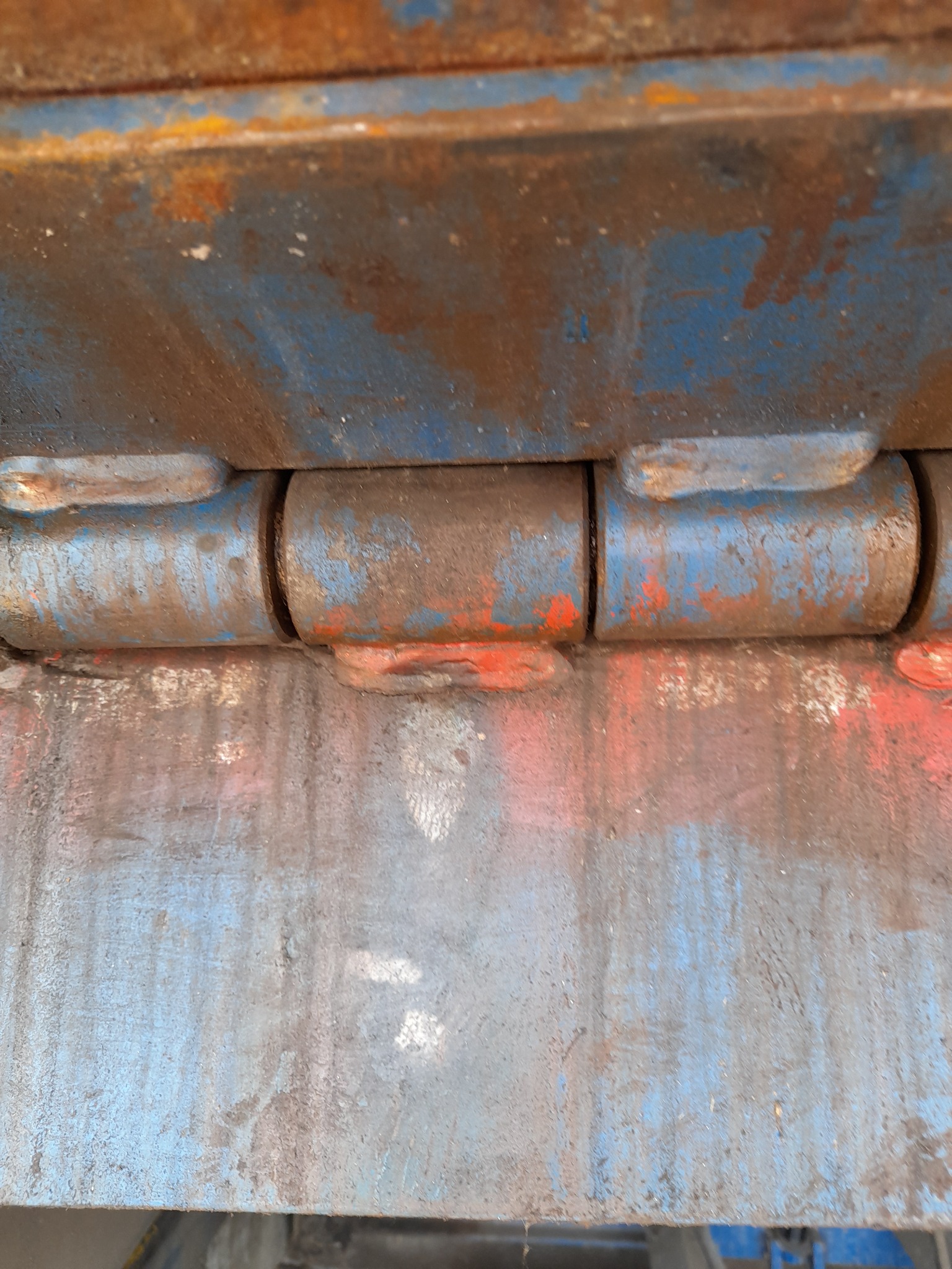 Zardzewiały zawias bramy przemysłowej, z widocznymi śladami farby niebieskiej i czerwonej, z bliska.