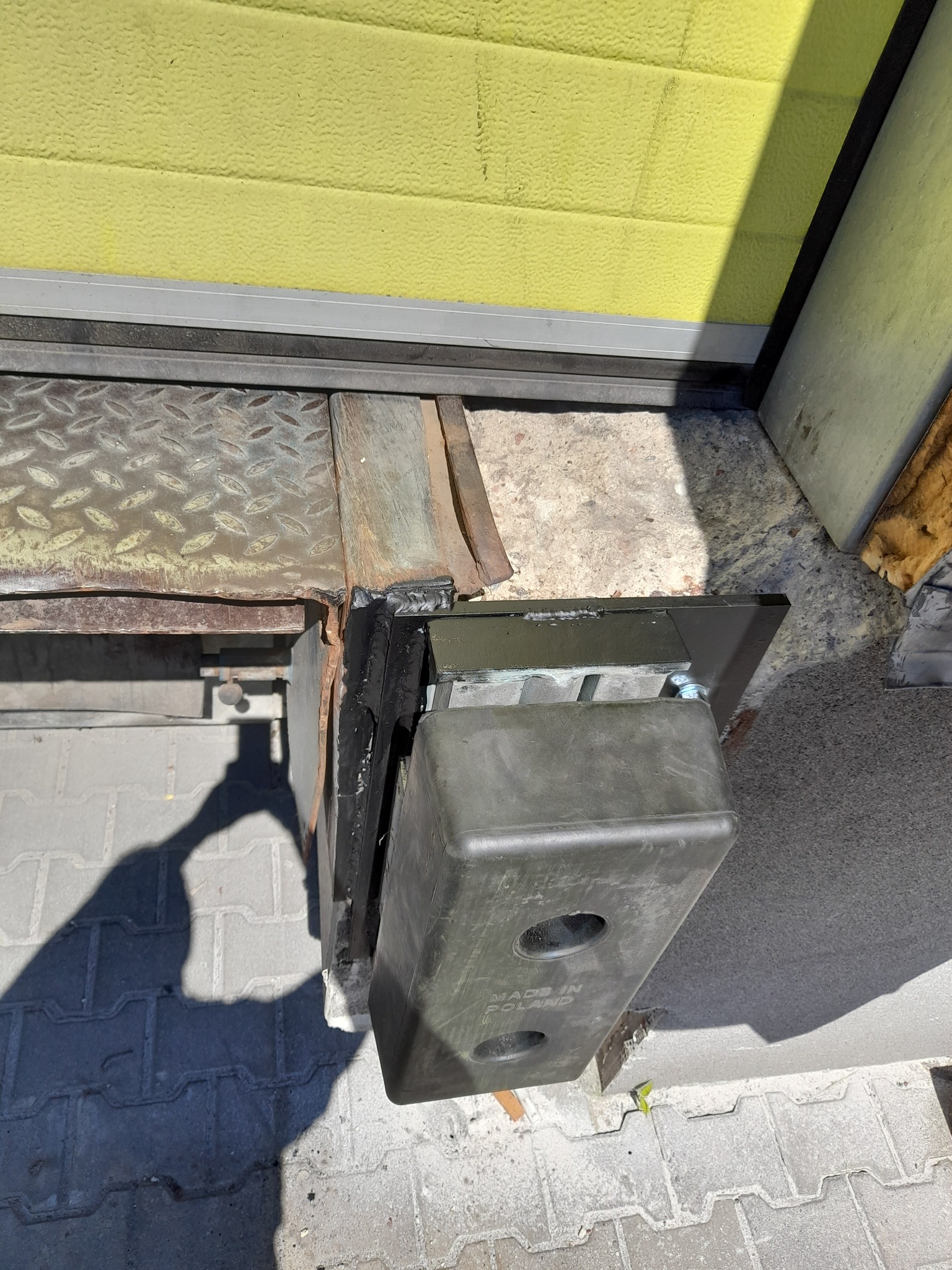 Szczegółowe ujęcie dolnej części bramy przemysłowej z widocznym mechanizmem i elementami montażowymi, z napisem 'Made in Poland' na obudowie.