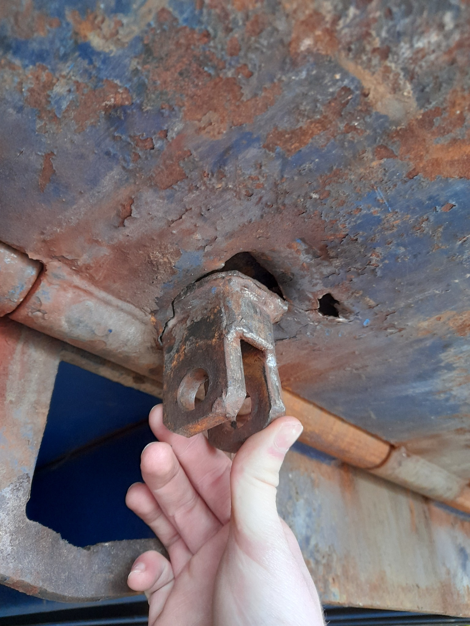 Zardzewiały uchwyt bramy przemysłowej, trzymany w dłoni, widoczne ślady korozji na konstrukcji bramy i ubytki farby.