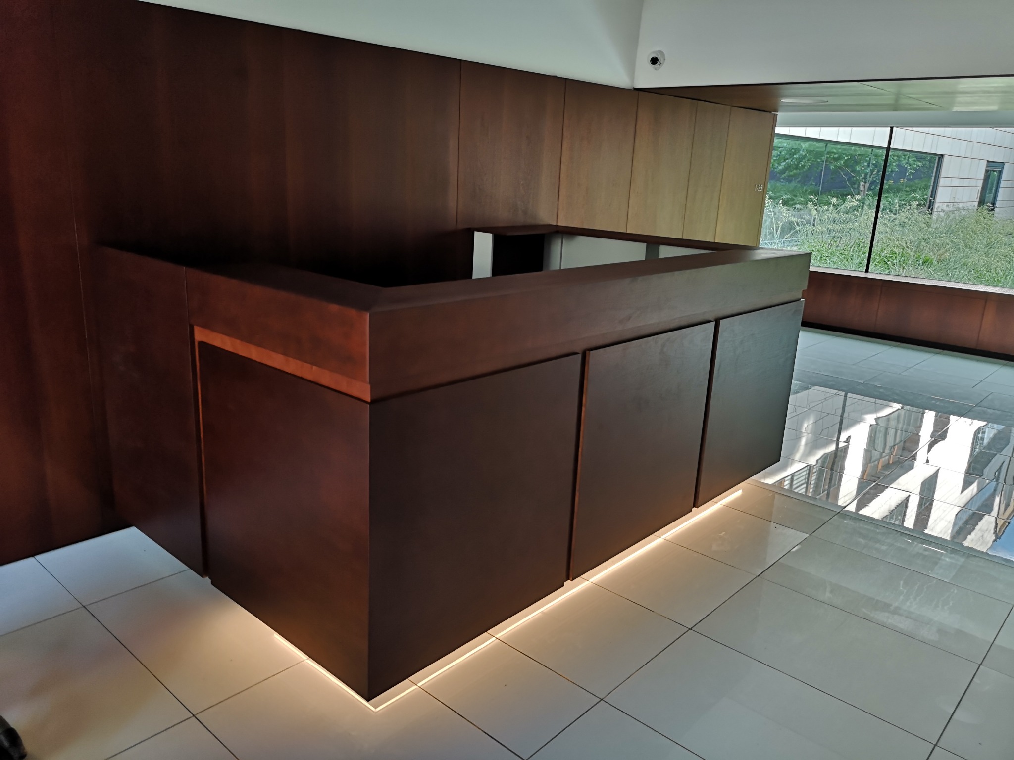 Nowoczesna, ciemnobrązowa recepcja z podświetleniem LED u dołu, widok na zewnątrz przez duże okno.