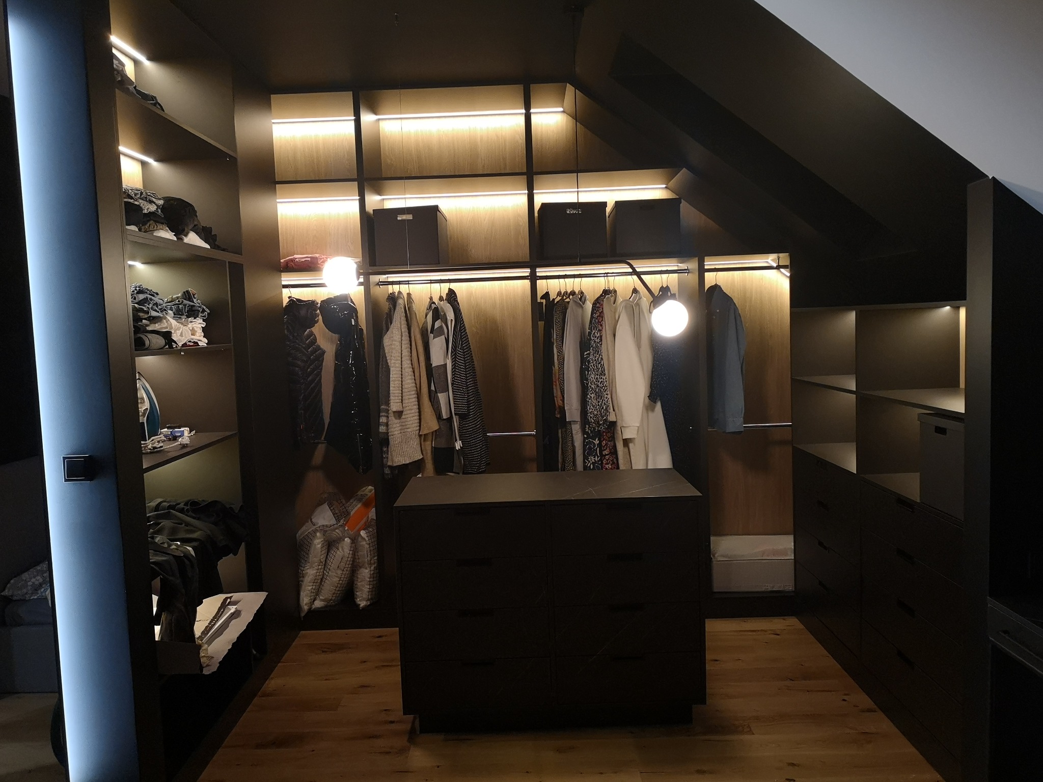 Czarna garderoba w zabudowie z oświetleniem LED, drewnianą podłogą i komodą z ciemnego kamienia