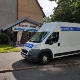 Samochód dostawczy firmy Nextbike z Kołobrzegu zaparkowany przed serwisem rowerowym Rower Sport Serwis Centrum. Na dachu i boku pojazdu widoczne logo i napis SERWIS.