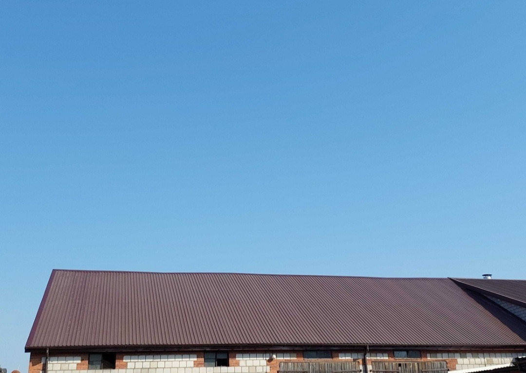 Nowy, brązowy dach z blachy trapezowej na budynku z białej cegły silikatowej, widoczny na tle błękitnego nieba.