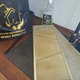 FIRMA SPSZĄTAJĄCA EFEKT RZESZOW - Dwa filtry okapu kuchennego, jeden z widocznym zabrudzeniem, obok torba i butelka ze środkiem czyszczącym firmy sprzątającej Efekt Rzeszów.