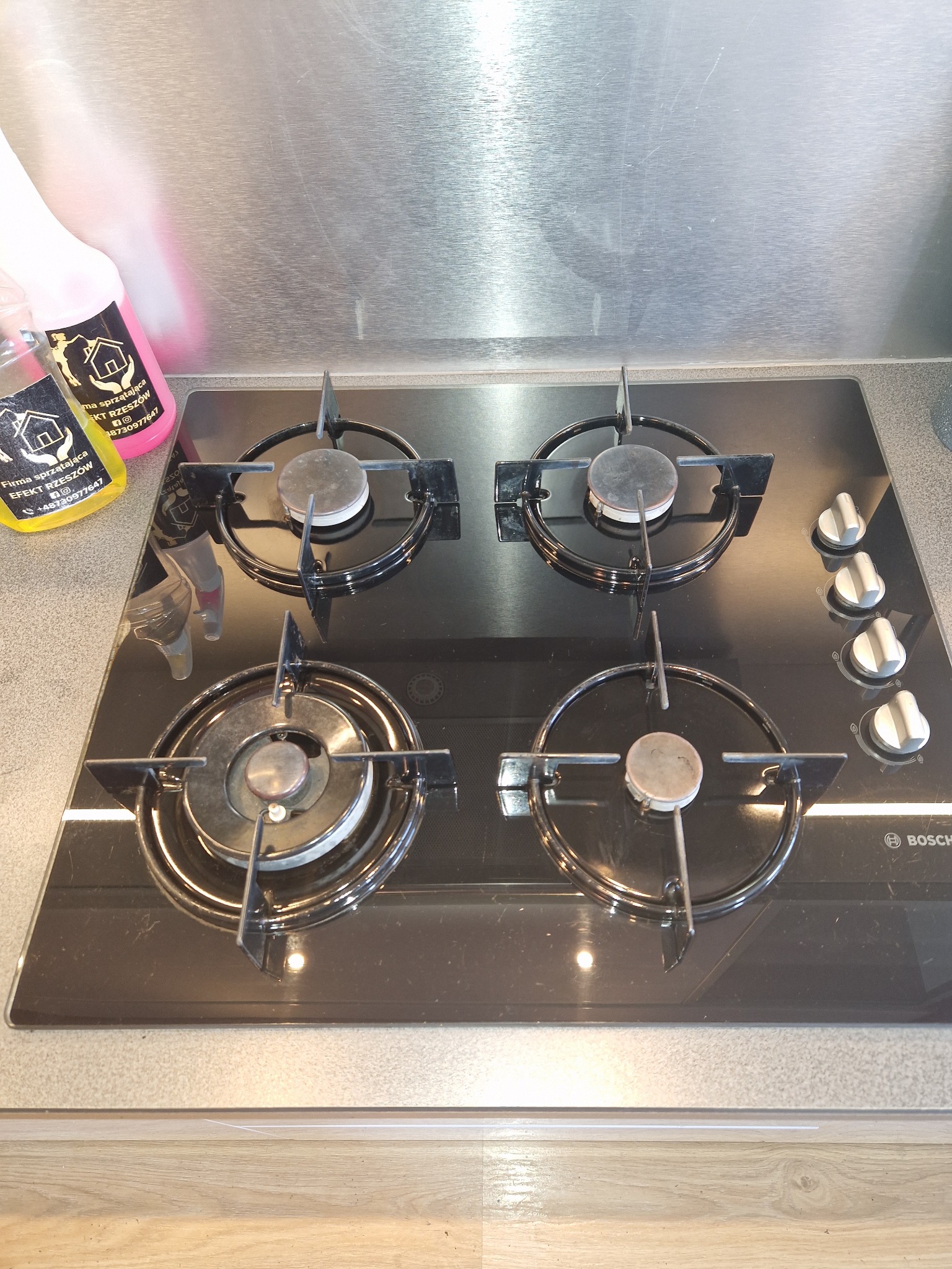 Czyszczenie płyty gazowej Bosch z czterema palnikami, widoczne środki czystości w tle, powierzchnia płyty błyszcząca, odbijająca światło.