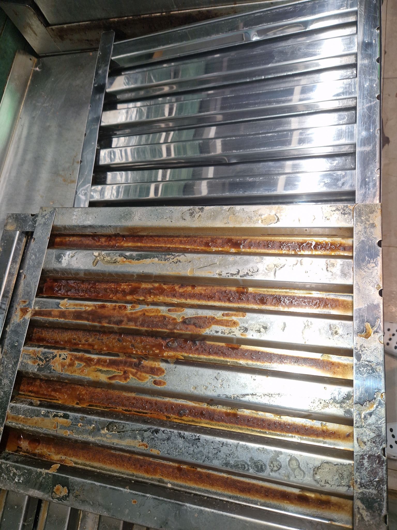 Dwa metalowe filtry przemysłowe, jeden czysty i błyszczący, drugi silnie zabrudzony zaschniętym tłuszczem i brudem, ukazujący kontrast przed i po czyszczeniu.