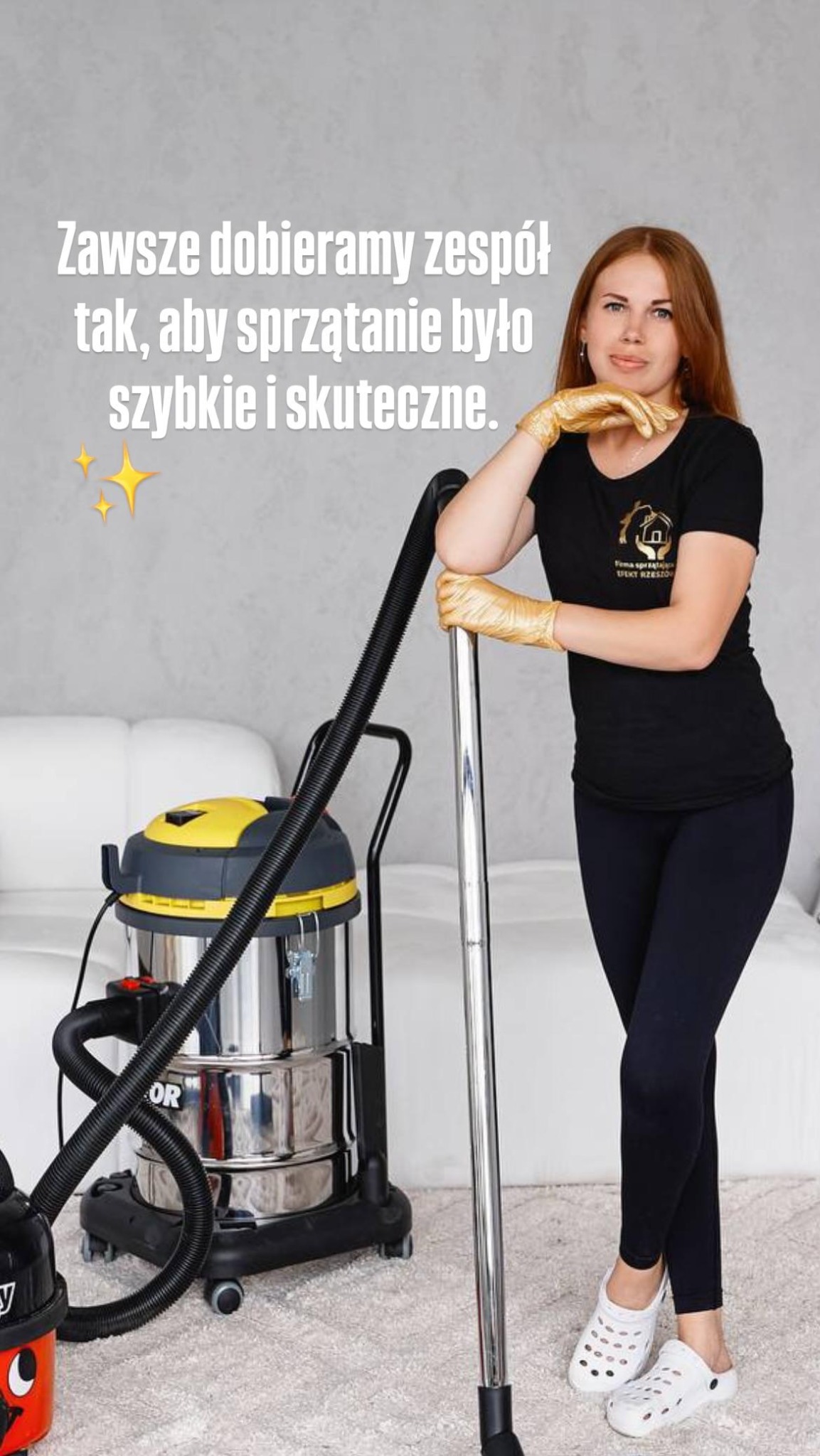 Kobieta w złotych rękawiczkach pozuje z odkurzaczem przemysłowym na tle sofy. Widoczny logotyp firmy sprzątającej na koszulce.
