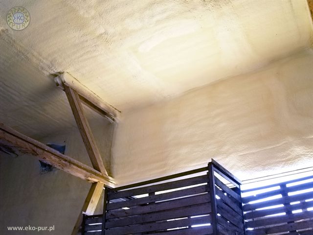 Wnętrze przechowalni z drewnianą konstrukcją i ścianami pokrytymi jednolitą warstwą izolacji natryskowej o porowatej strukturze.