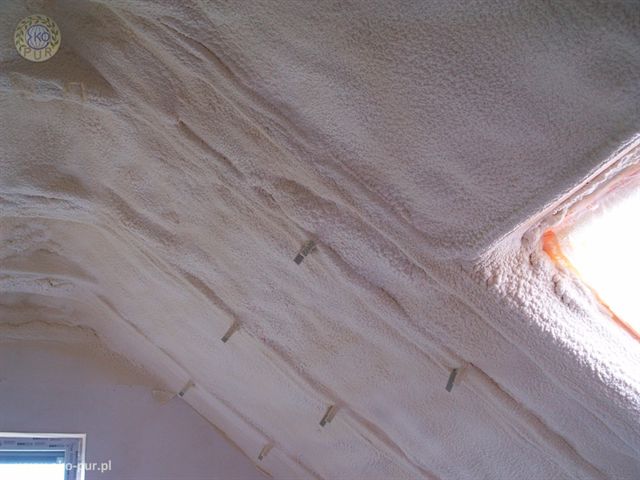 Poddasze ocieplone pianą, widoczne krokwie i okno dachowe, jasna, równomierna warstwa izolacji.