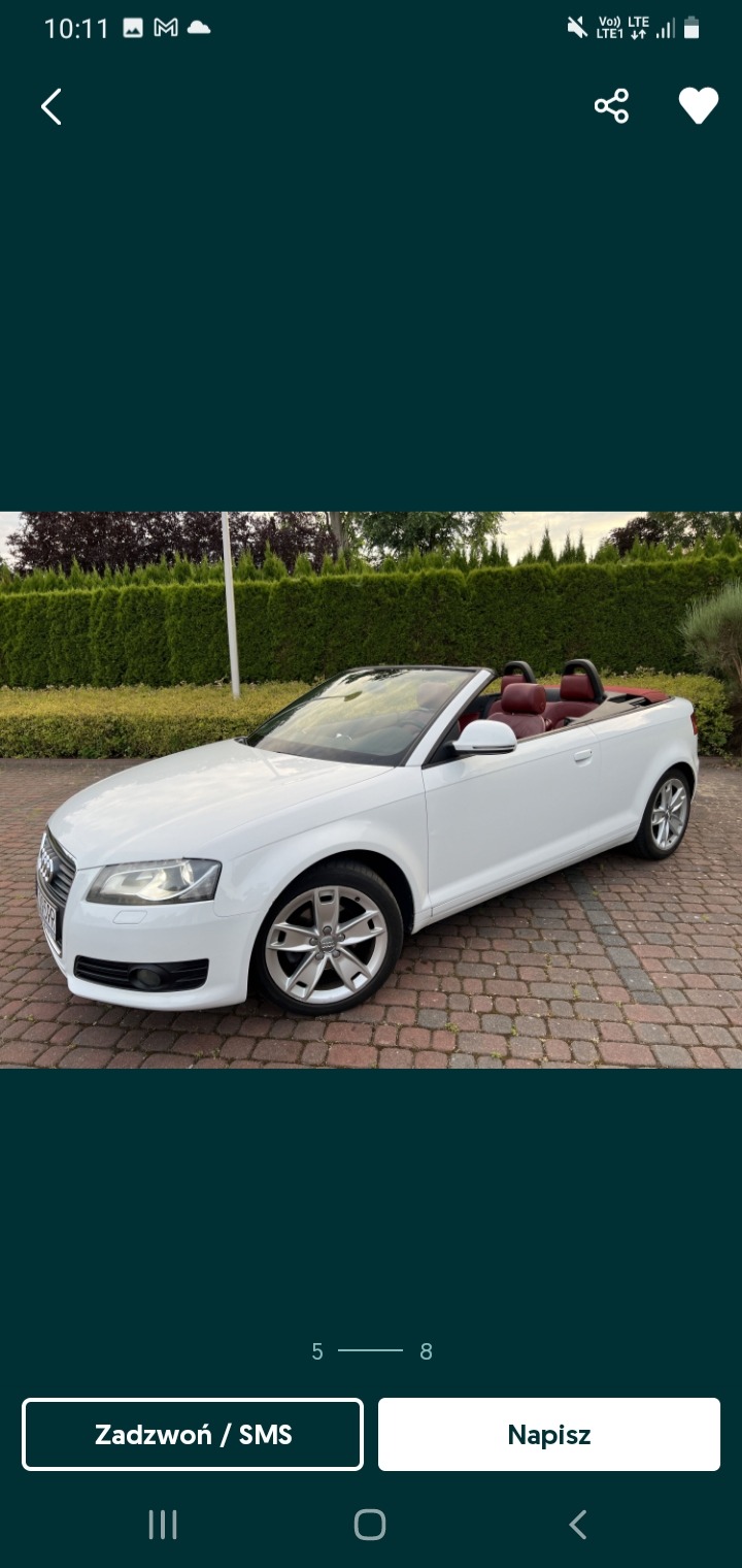 Biały kabriolet Audi z czerwonymi skórzanymi siedzeniami, zaparkowany na brukowanej drodze przed zielonym żywopłotem.