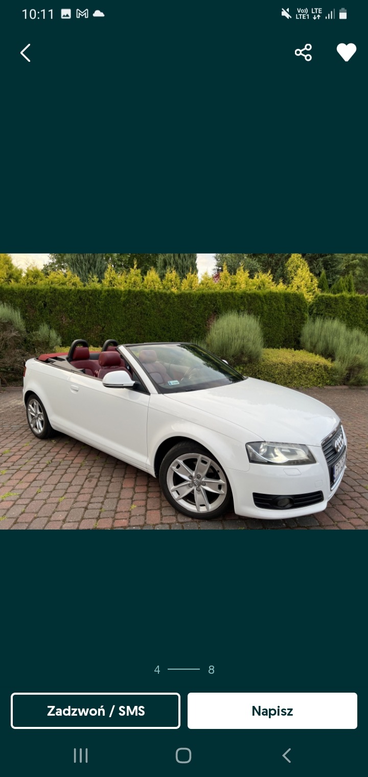 Biały kabriolet Audi z bordową skórzaną tapicerką, zaparkowany na brukowanym podjeździe przed zielonym żywopłotem.