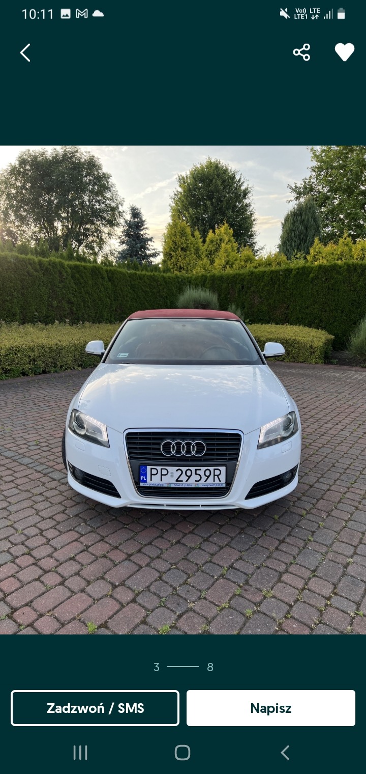 Biały kabriolet Audi z czerwonym dachem zaparkowany na brukowanym podjeździe przed zadbanym żywopłotem w słoneczny dzień.