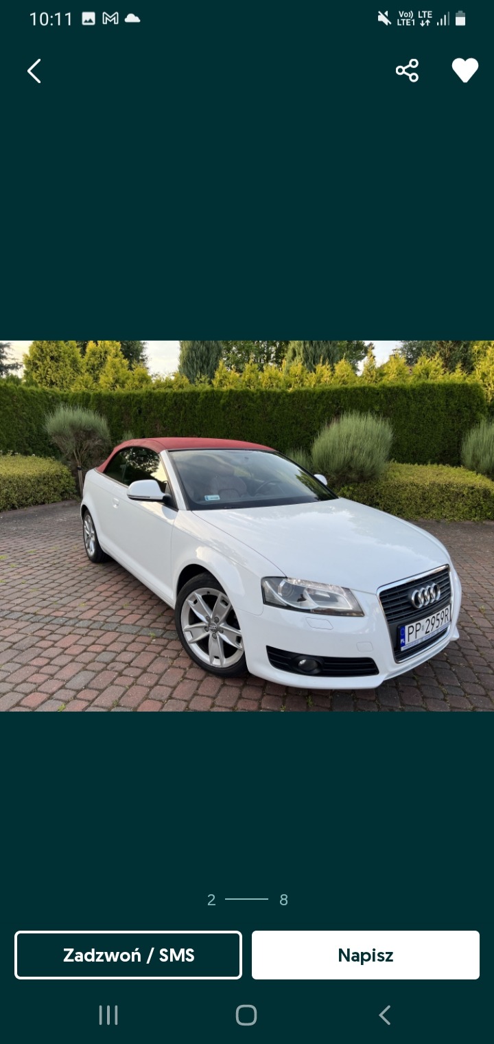 Biały kabriolet Audi z czerwonym dachem zaparkowany na brukowanym podjeździe przed zielonym żywopłotem.