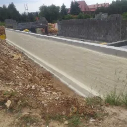 Świeżo zaizolowane pianką PUR fundamenty budynku w trakcie budowy, widoczne bloczki betonowe i ziemia.