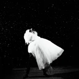 Czarno-białe, artystyczne zdjęcie pary młodej w tańcu pod latarnią podczas opadów. Panna młoda w zwiewnej sukni i futrze, pan młody w ciemnym garniturze. Nastrojowe oświetlenie.