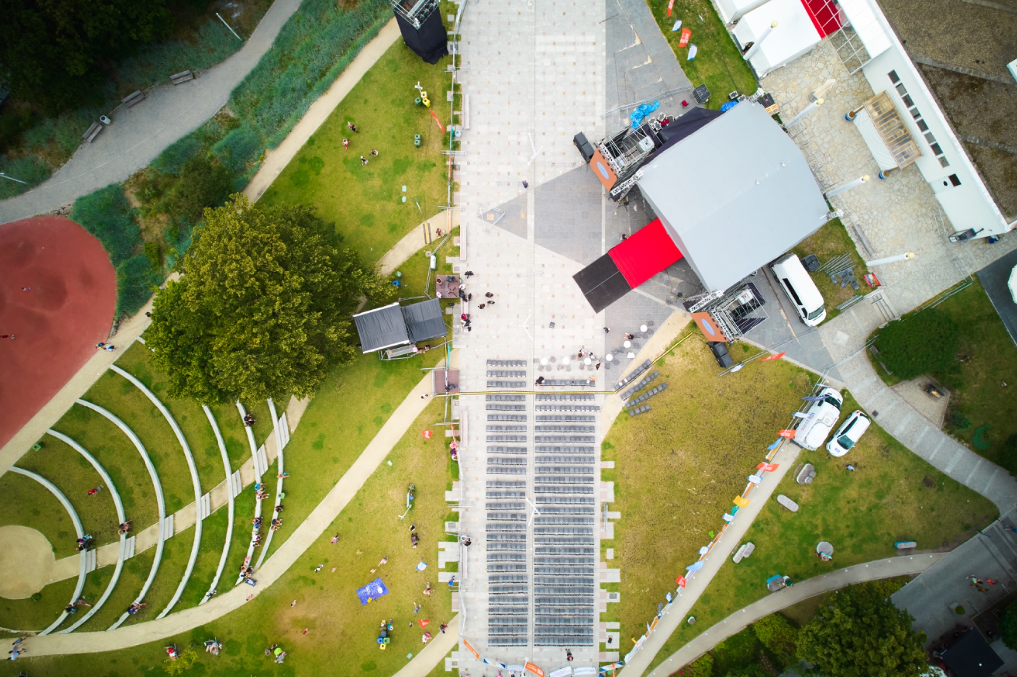Widok z lotu ptaka na teren imprezy plenerowej z rozstawioną sceną, nagłośnieniem, amfiteatrem i zapleczem technicznym oraz licznymi uczestnikami.
