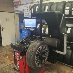 Wyważarka Hunter GSP9700 z oponą na stanowisku, monitor z symulacją wyważania, w tle rząd opon na półkach i tablica Michelin w warsztacie samochodowym.