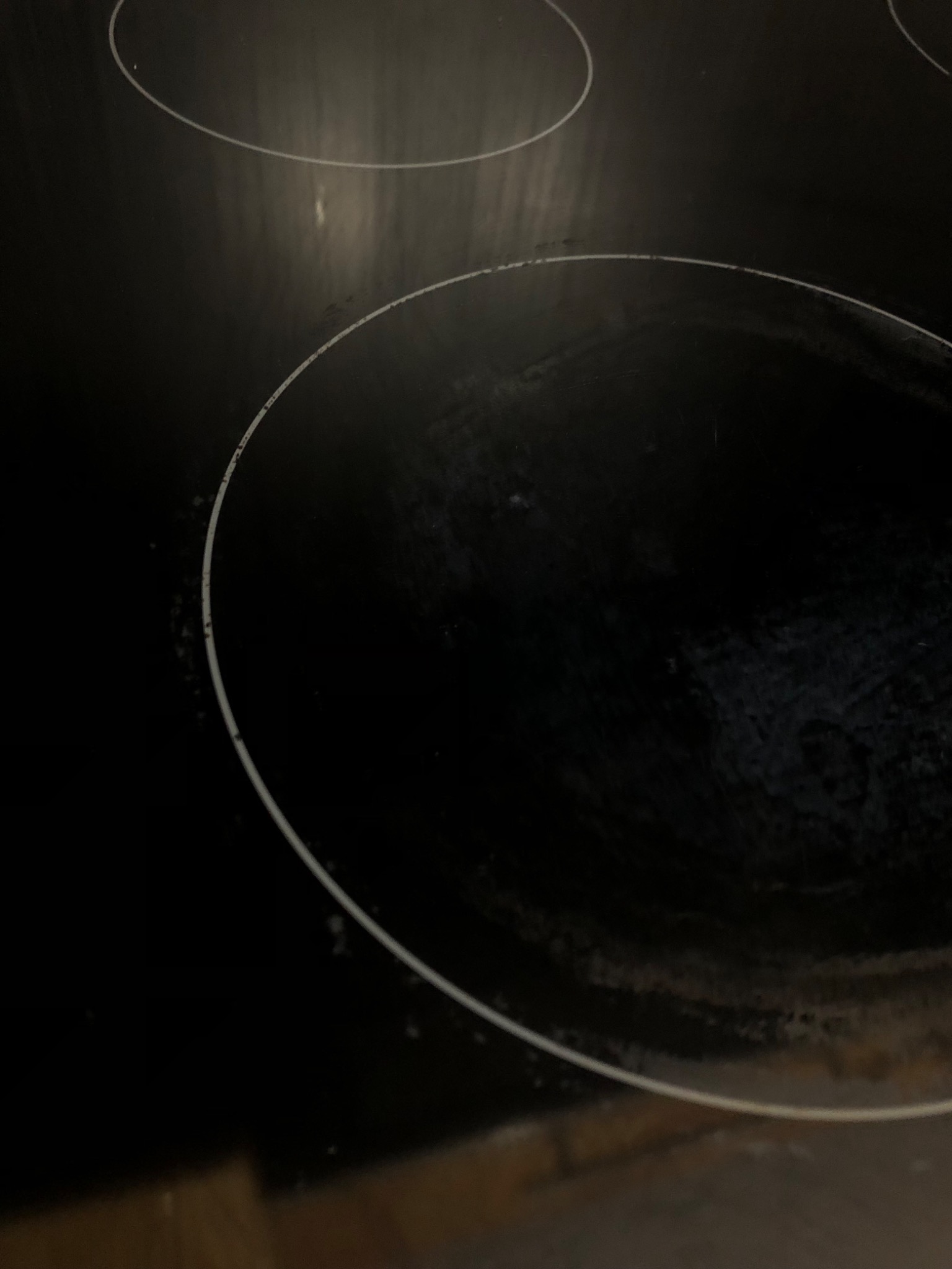 Zabrudzona płyta indukcyjna z widocznymi śladami po gotowaniu, wymagająca czyszczenia, ujęcie pod kątem.