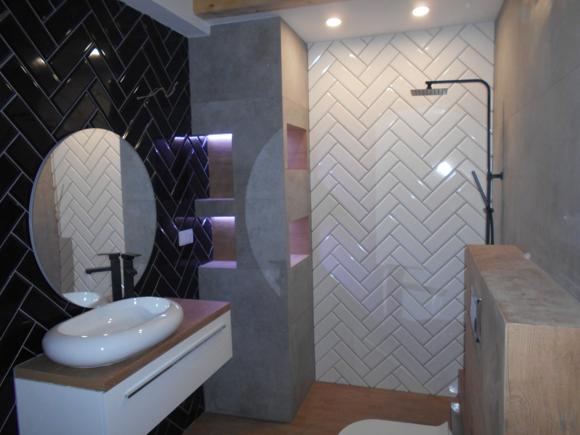 Nowoczesna łazienka w Giżycku z czarno-białymi płytkami ułożonymi w jodełkę, owalną umywalką nablatową i wnękami z podświetleniem LED.