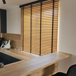 Adam Turowski OKNARO - Drewniane żaluzje poziome w kuchni z blatem i krzesłami barowymi. Naturalne światło podkreśla strukturę drewna. Minimalistyczny design.