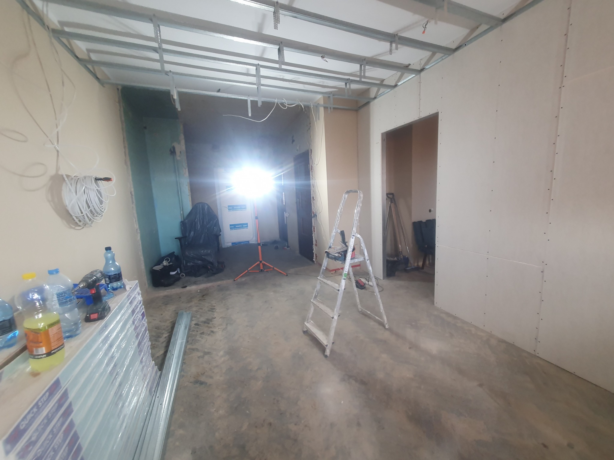 Montaż płyt kartonowo-gipsowych na ścianach i suficie w Tczewie, widoczny metalowy stelaż sufitowy, drabina, lampa budowlana i zapas płyt.