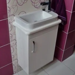 Biała umywalka z szafką w łazience z fioletowymi akcentami na ścianach i ręczniku