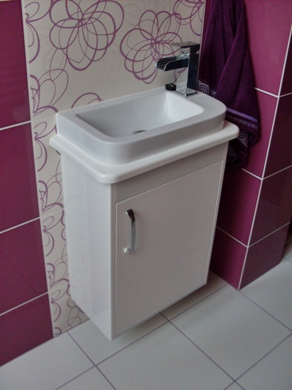 Biała umywalka z szafką w łazience z fioletowymi akcentami na ścianach i ręczniku