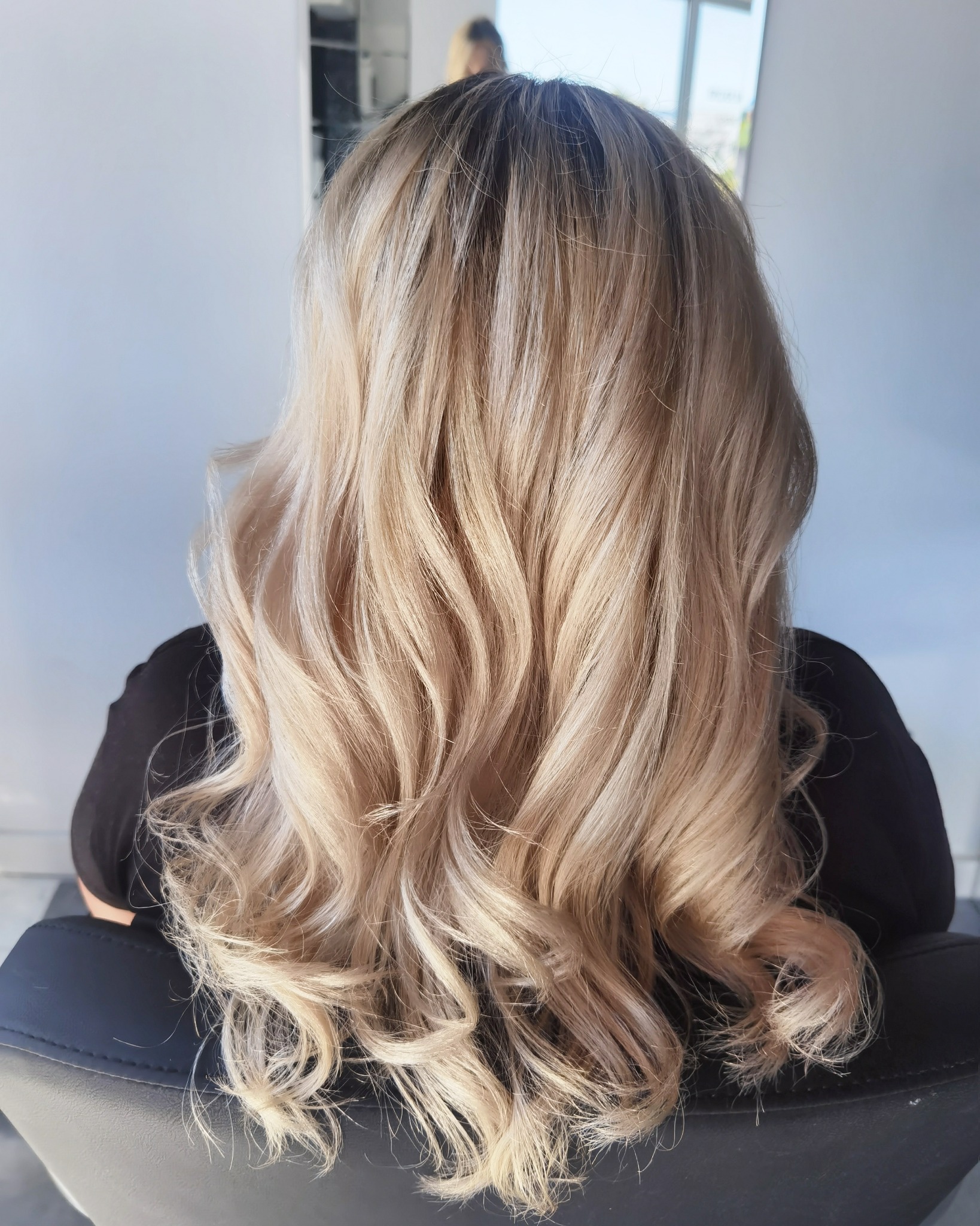 Widok z tyłu na długie, blond włosy z delikatnymi falami, świeżo po stylizacji w salonie, z widocznym odrostem u nasady.